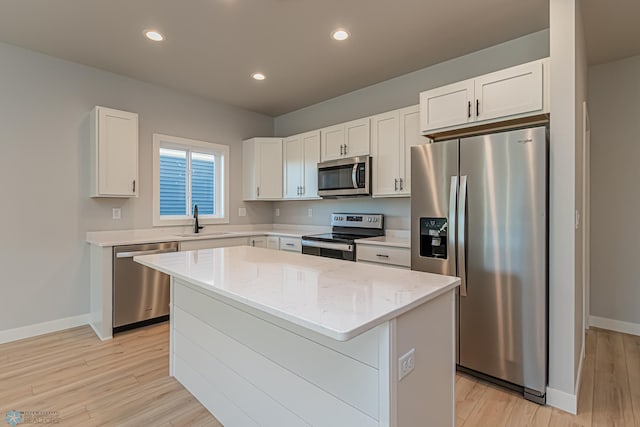 kitchen featuring light wood-style flooring, appliances with stainless steel finishes, a sink, baseboards, and a center island