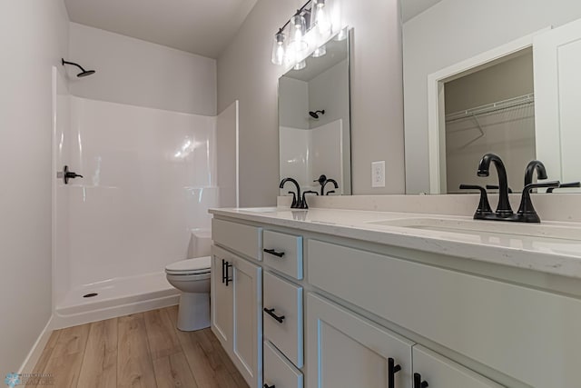 full bathroom with a sink, toilet, double vanity, walk in shower, and wood finished floors