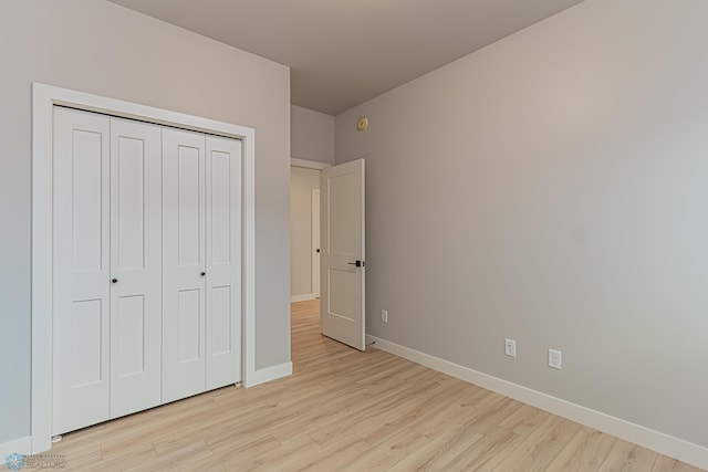 unfurnished bedroom featuring light wood-type flooring, a closet, and baseboards