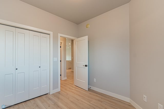 unfurnished bedroom featuring a closet, light wood-style flooring, and baseboards