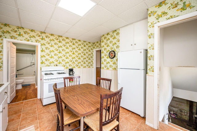 dining area featuring wainscoting, light tile patterned floors, a drop ceiling, and wallpapered walls