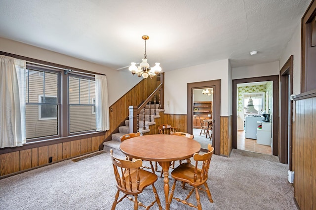 carpeted dining room featuring washer / clothes dryer, wood walls, a wainscoted wall, a notable chandelier, and stairs