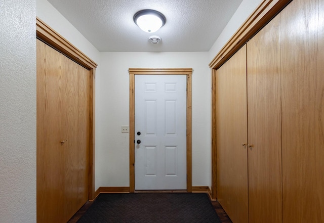 doorway with a textured ceiling, dark colored carpet, and baseboards
