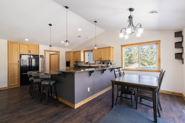 kitchen featuring freestanding refrigerator, a kitchen breakfast bar, vaulted ceiling, light brown cabinetry, and dark wood-style flooring