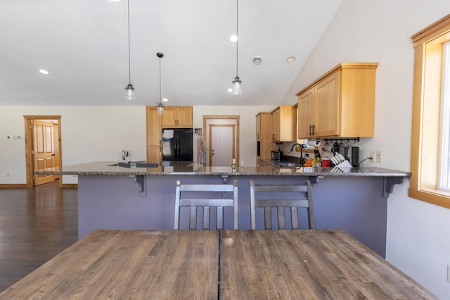kitchen featuring freestanding refrigerator, a sink, a peninsula, stone counters, and dark wood-type flooring