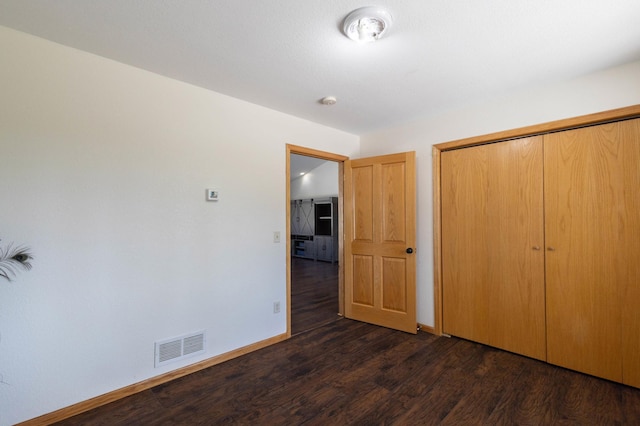 unfurnished bedroom with dark wood-style floors, baseboards, and a closet