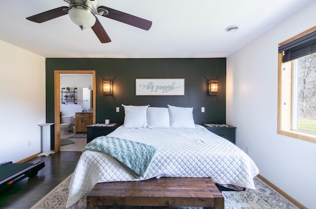 bedroom with wood finished floors, baseboards, ceiling fan, ensuite bath, and an accent wall