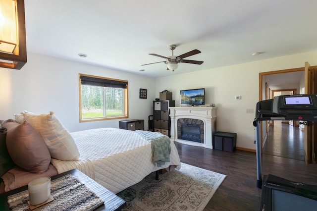 bedroom with a glass covered fireplace, dark wood-style floors, ceiling fan, and baseboards