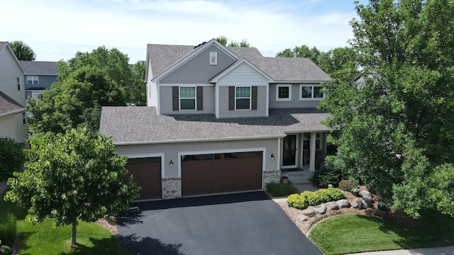 view of front of home with a shingled roof, an attached garage, driveway, and stone siding