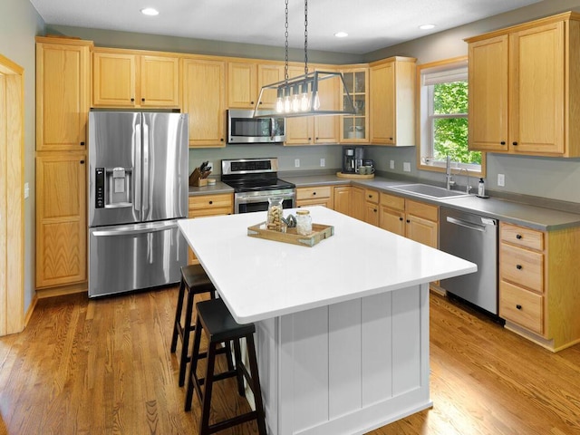 kitchen featuring appliances with stainless steel finishes, a sink, light brown cabinetry, a kitchen breakfast bar, and a kitchen island