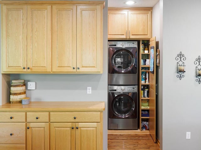 laundry room featuring stacked washer / drying machine, cabinet space, and wood finished floors
