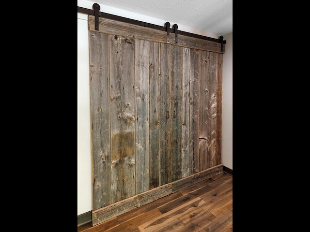 detailed view of a barn door, a textured ceiling, wood finished floors, and baseboards
