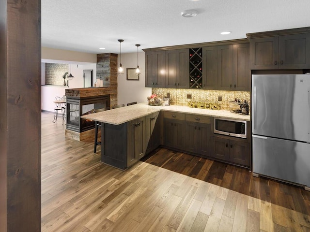 kitchen with stainless steel appliances, backsplash, a peninsula, dark wood-type flooring, and pendant lighting