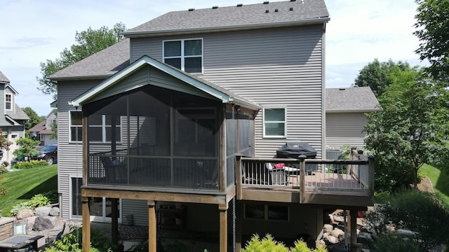 rear view of property featuring a sunroom, a shingled roof, and a wooden deck