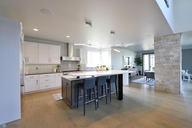 kitchen featuring wall chimney range hood, light wood-type flooring, white cabinetry, and a breakfast bar