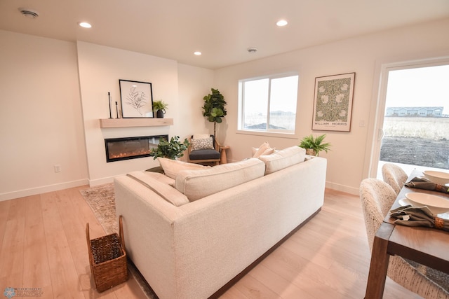 living room with recessed lighting, baseboards, a glass covered fireplace, and light wood-style flooring