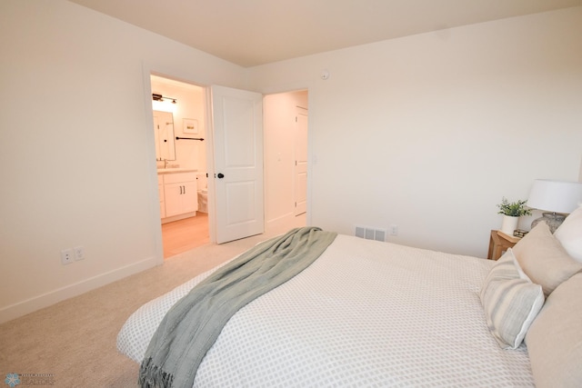 bedroom with visible vents, baseboards, light colored carpet, a sink, and ensuite bath