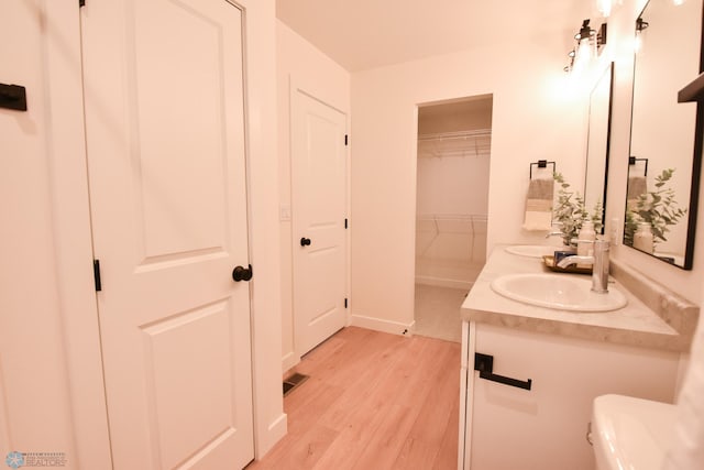 full bath with double vanity, a sink, wood finished floors, and toilet
