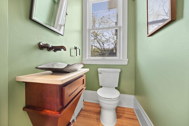 half bath with baseboards, wood finished floors, a healthy amount of sunlight, and toilet