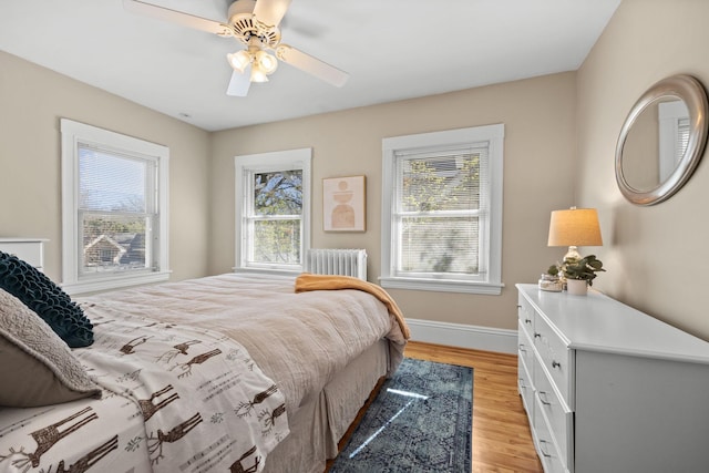 bedroom with radiator heating unit, baseboards, a ceiling fan, and light wood finished floors