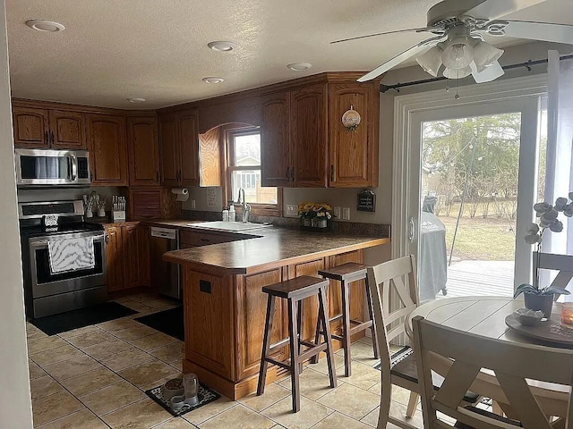 kitchen featuring ceiling fan, appliances with stainless steel finishes, a sink, a kitchen breakfast bar, and a peninsula