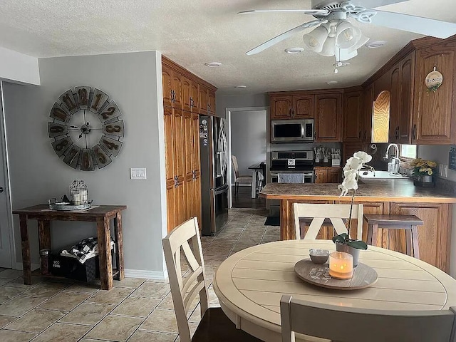 kitchen featuring appliances with stainless steel finishes, a sink, a textured ceiling, a ceiling fan, and a peninsula