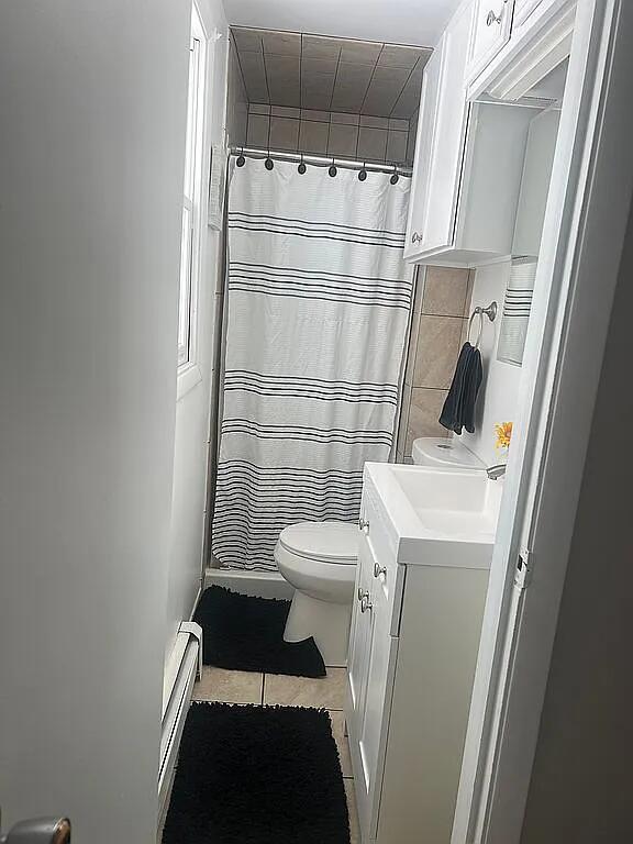 full bathroom featuring vanity, toilet, a shower with shower curtain, baseboard heating, and tile patterned floors