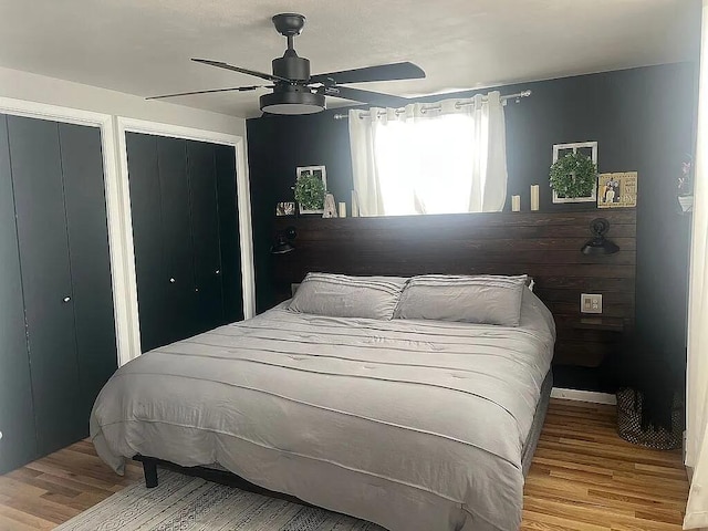 bedroom with a ceiling fan, multiple closets, and wood finished floors