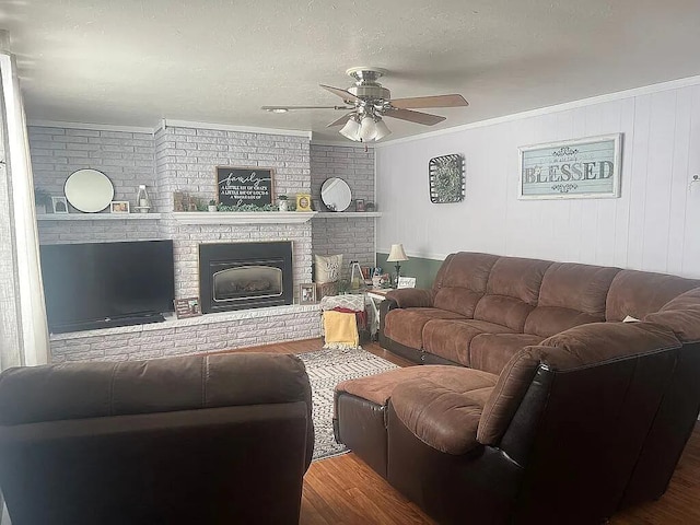 living room with crown molding, a ceiling fan, a brick fireplace, and wood finished floors
