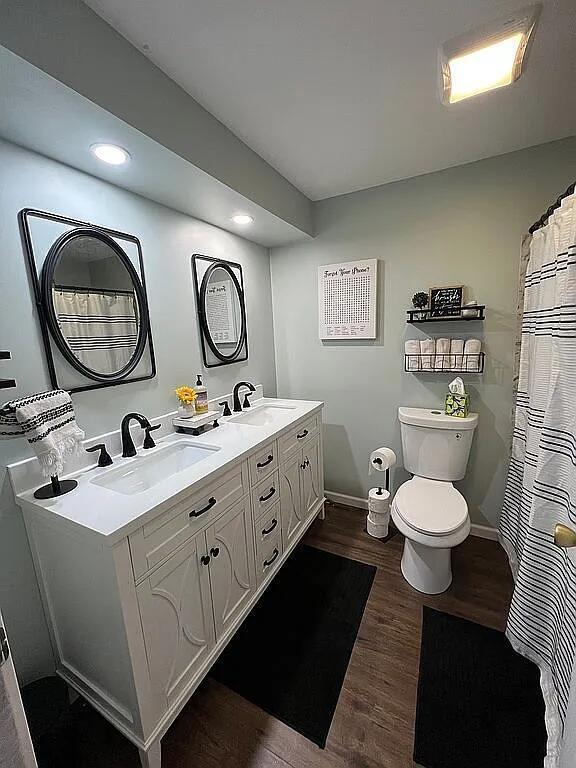 bathroom with double vanity, wood finished floors, a sink, toilet, and recessed lighting