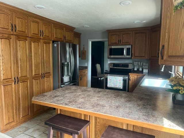 321 Meredith Rd, Albert Lea, MN 56007 - kitchen featuring appliances with stainless steel finishes, a peninsula, brown cabinetry, a breakfast bar, and a sink