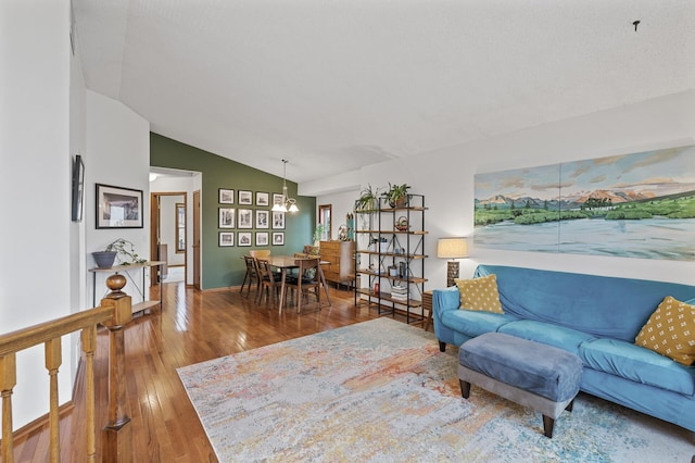 living area featuring an inviting chandelier, hardwood / wood-style flooring, vaulted ceiling, and baseboards