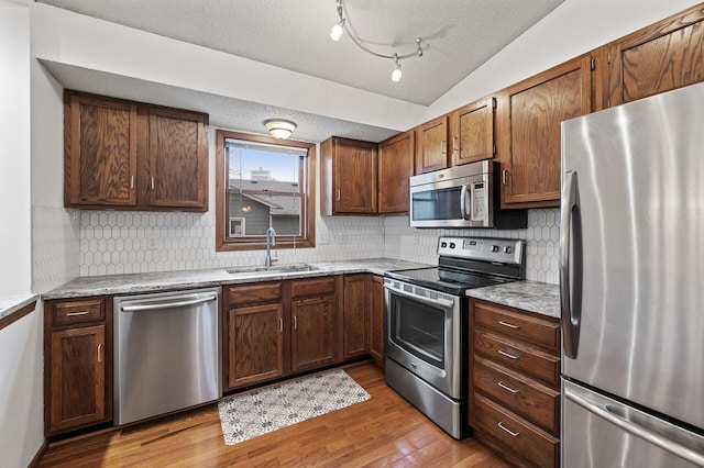 kitchen with a sink, light wood-style flooring, backsplash, a textured ceiling, and appliances with stainless steel finishes