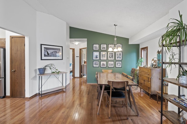 dining space featuring wood finished floors, high vaulted ceiling, a notable chandelier, and baseboards