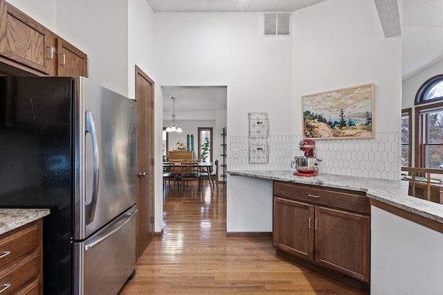 kitchen featuring tasteful backsplash, freestanding refrigerator, light wood-type flooring, visible vents, and a towering ceiling