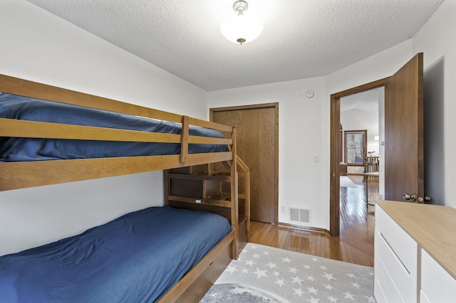 bedroom with a textured ceiling, visible vents, and wood finished floors