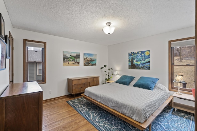 bedroom featuring baseboards, light wood-style floors, and a textured ceiling