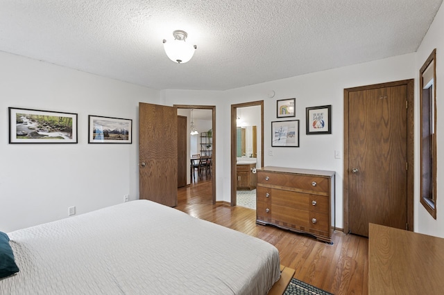 bedroom featuring connected bathroom, a textured ceiling, and wood finished floors