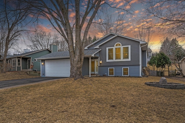 split level home with aphalt driveway, a lawn, a chimney, an attached garage, and fence