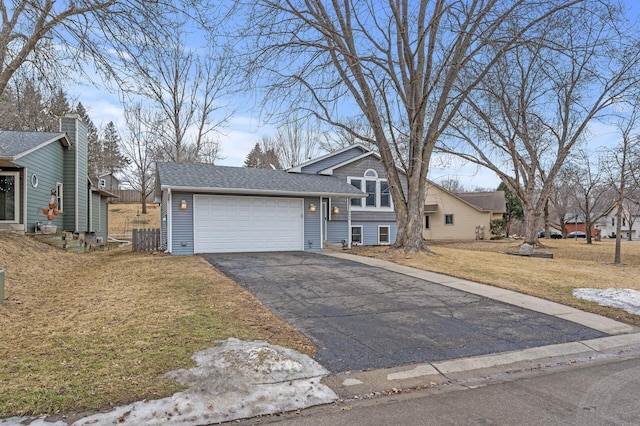 split level home featuring a garage, a shingled roof, a front lawn, and driveway