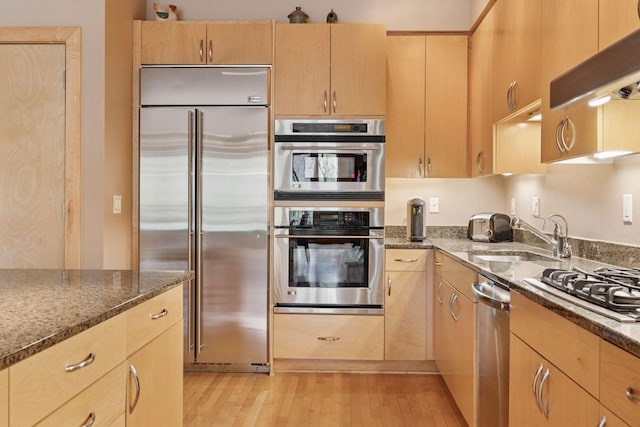 401 2nd St Unit 202, Minneapolis, MN 55401 - kitchen featuring light brown cabinets, dark stone counters, light wood-style floors, appliances with stainless steel finishes, and a sink