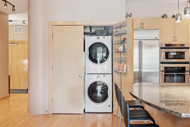 401 2nd St Unit 202, Minneapolis, MN 55401 - clothes washing area featuring visible vents, stacked washing maching and dryer, light wood-type flooring, track lighting, and laundry area