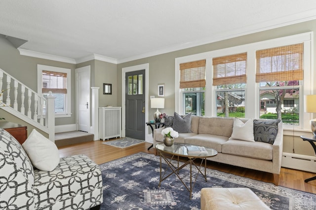 living area with a baseboard heating unit, wood finished floors, crown molding, stairs, and baseboards
