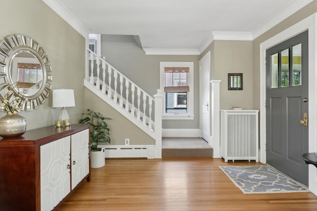 foyer entrance featuring radiator, baseboard heating, light wood-type flooring, ornamental molding, and stairs