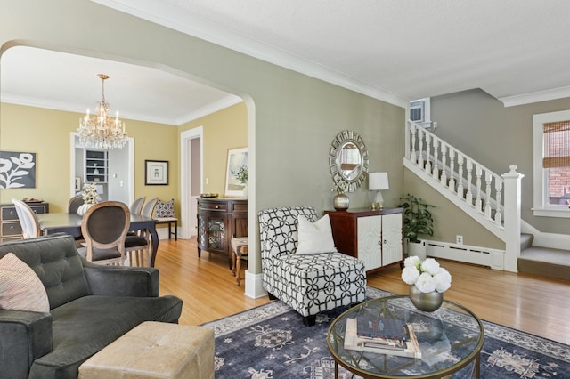 living room with baseboard heating, wood finished floors, a chandelier, crown molding, and arched walkways