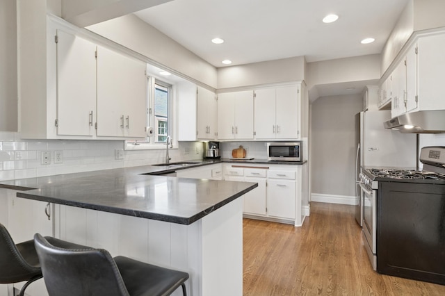 kitchen with stainless steel appliances, under cabinet range hood, a sink, a peninsula, and white cabinetry