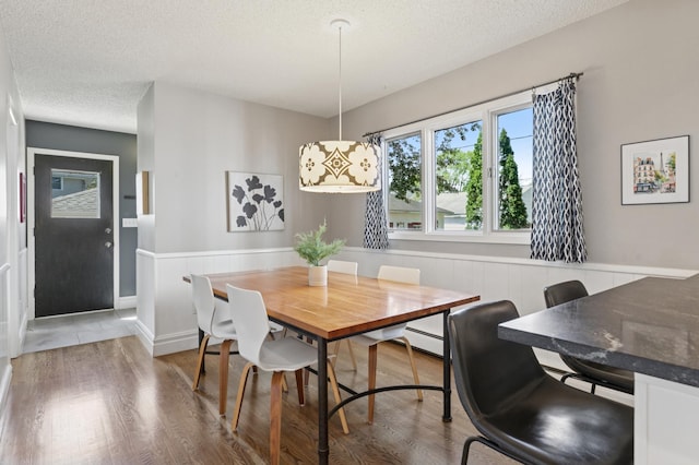 dining area with wood finished floors, a textured ceiling, and wainscoting