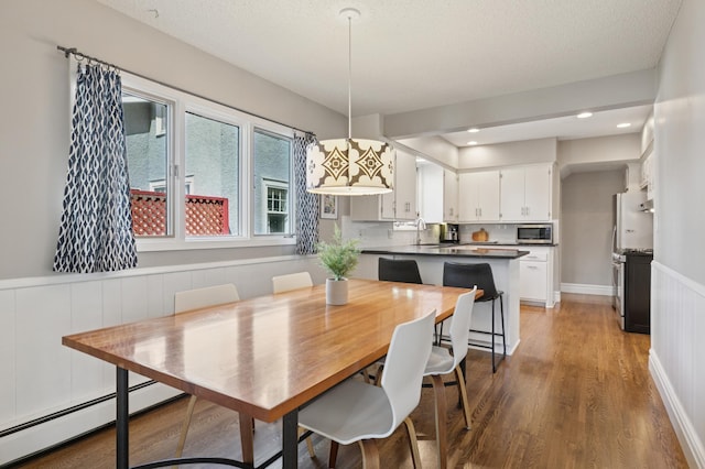 dining space featuring a baseboard heating unit, wood finished floors, a wainscoted wall, and recessed lighting