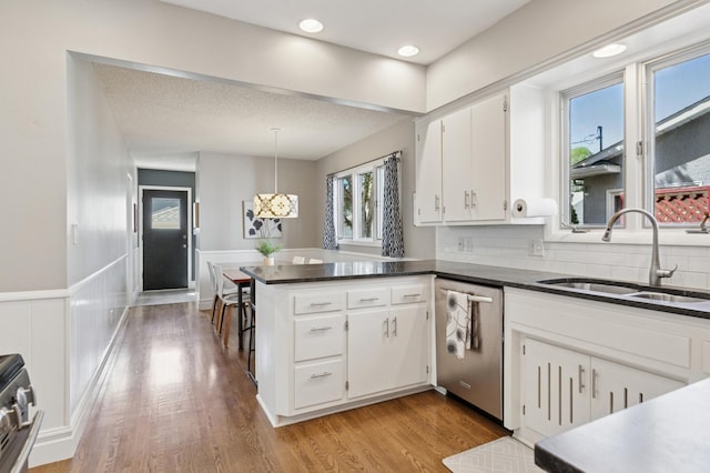 kitchen featuring a sink, stainless steel appliances, a peninsula, dark countertops, and white cabinetry