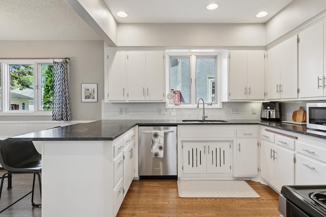 kitchen with stainless steel appliances, a sink, a peninsula, white cabinetry, and recessed lighting